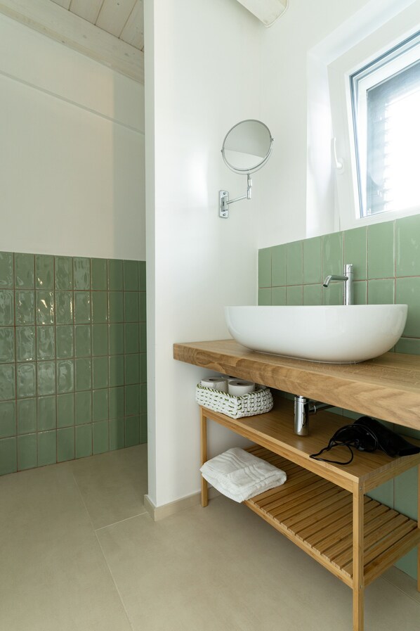 A bathroom with a white sink, green tiles, a wooden vanity, and a mirror.