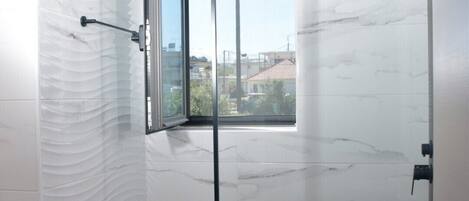 A modern bathroom with a glass shower door, a white sink, and a view of the city through the window.