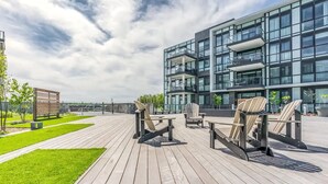 Un espace extérieur moderne, aménagé avec un plancher en bois et des fauteuils Adirondack, jouxtant un bâtiment contemporain doté de balcons.