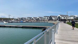 Une promenade en bord de mer avec une passerelle en bois, des bateaux amarrés dans la marina et des bâtiments modernes en arrière-plan.