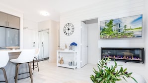 Un salon moderne avec une cheminée, un coin repas avec des chaises blanches, une console blanche agrémentée d’objets décoratifs et une grande horloge murale.