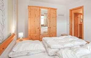A bedroom with a wooden wardrobe, a bedside table with a lamp, and a bed with white bedding.