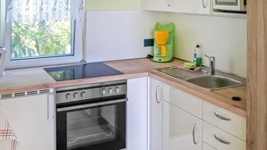 A compact kitchen with a stove, sink, and a window with curtains. - Lovely home in Lychen with sauna (Lychen)