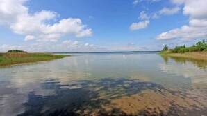 Een kalme rivier met helder water, omgeven door grasoevers en bomen onder een blauwe lucht met wolken.