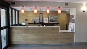 A reception desk with a wooden finish, overhead lighting, and framed artwork on the wall.