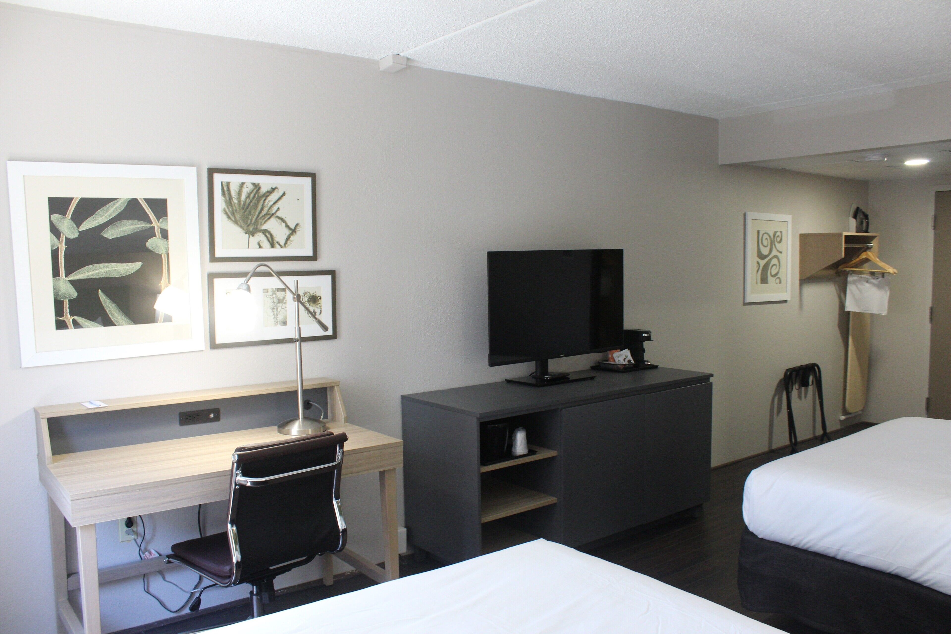 Een hotelkamer met een bureau, een televisie, twee bedden en kunstwerken aan de muur.