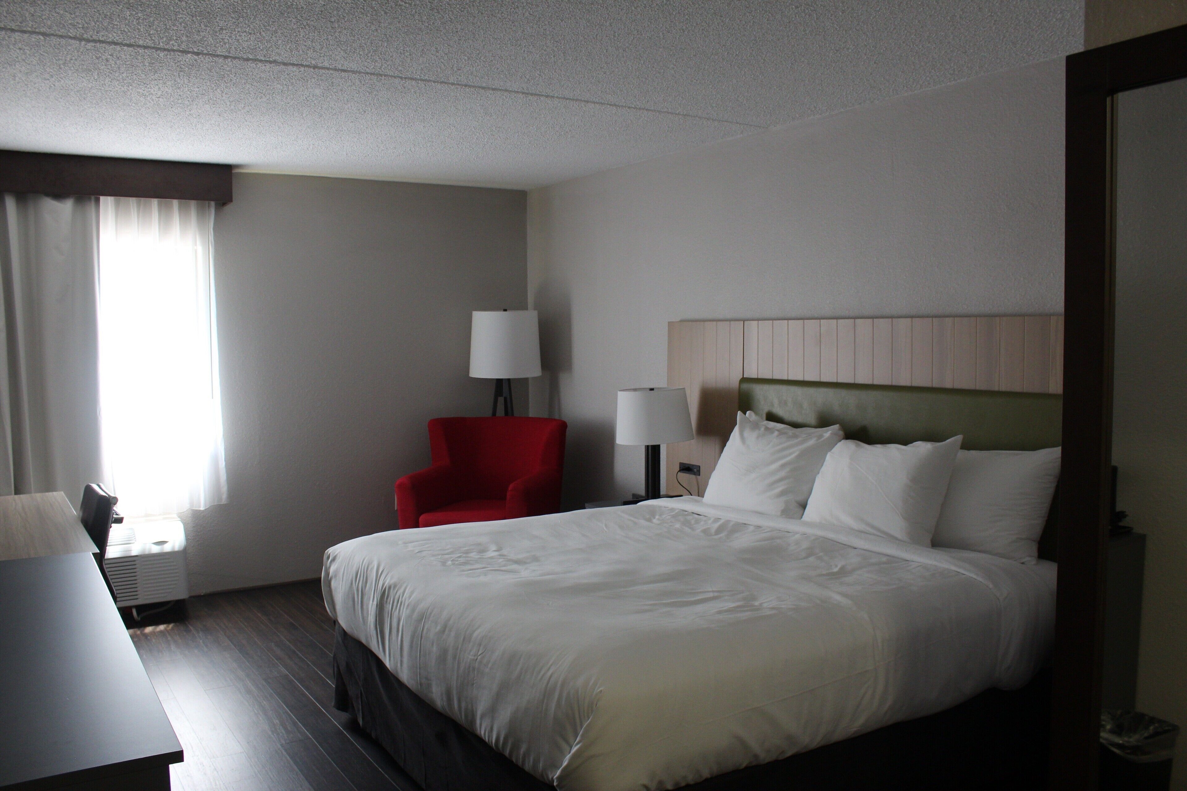 A hotel room with a large bed, a red armchair, a desk, and a lamp.