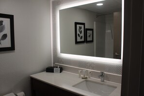 A bathroom with a large mirror, a sink, and a vanity. There are framed pictures on the wall and toiletries on the counter.