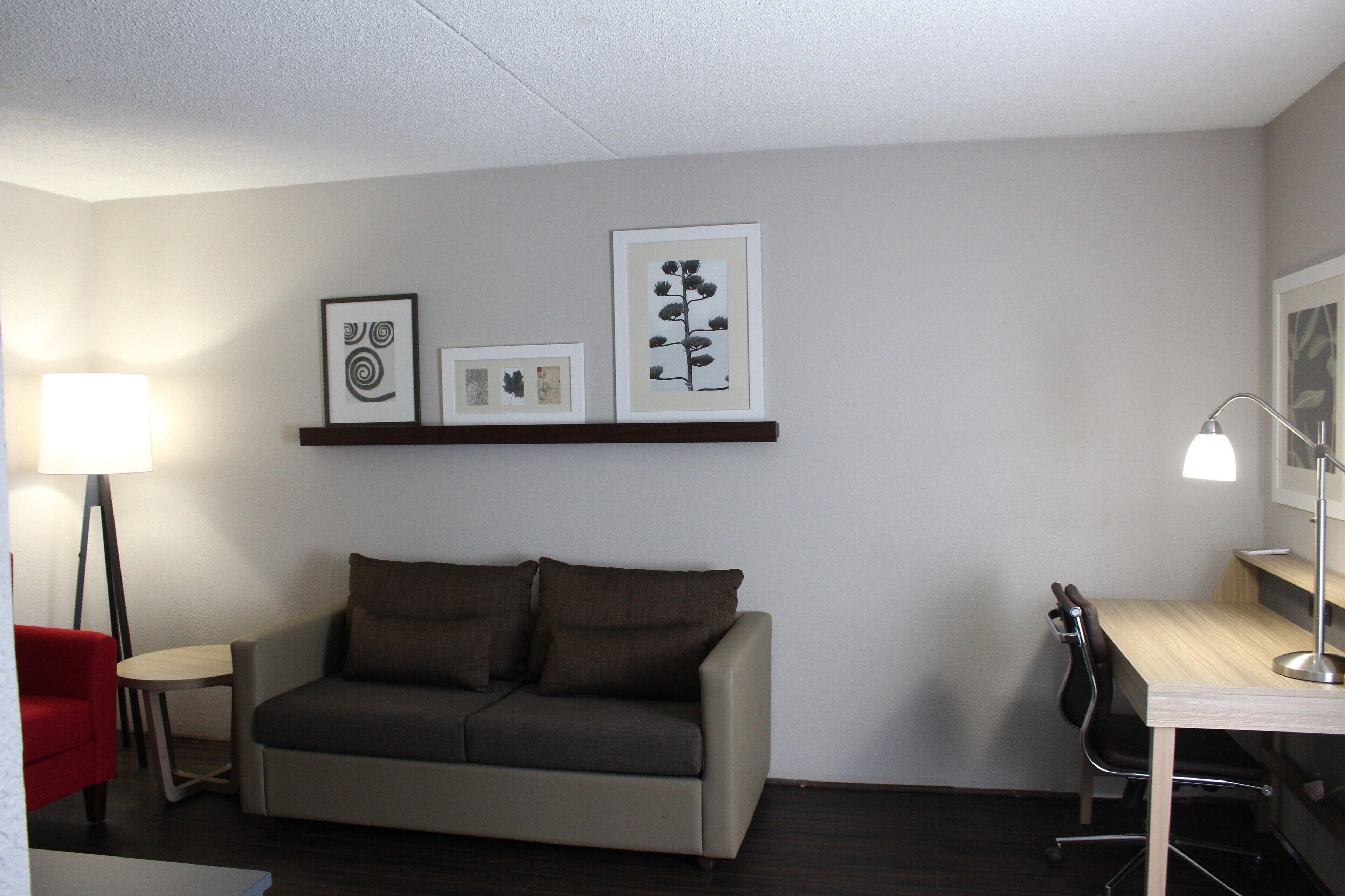 A modern room with a sofa, a desk, and a chair. There are framed pictures on the wall.