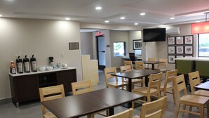 A dining area with multiple tables and chairs, a coffee station, and a television mounted on the wall.