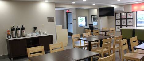 A dining area with multiple tables and chairs, a coffee station, and a television mounted on the wall.