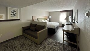 A hotel room with a sofa, a bed, a desk, and a lamp.
