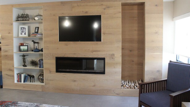 A modern living room with a wooden wall, a flat-screen TV, a fireplace, and a bookshelf.