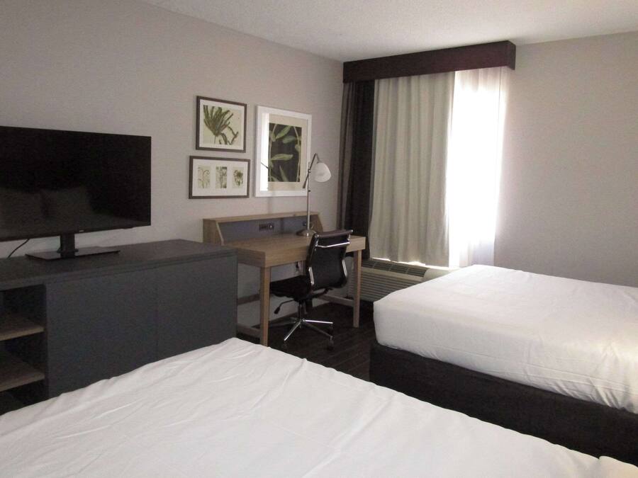 A hotel room with two beds, a desk, a television, and framed artwork on the wall.
