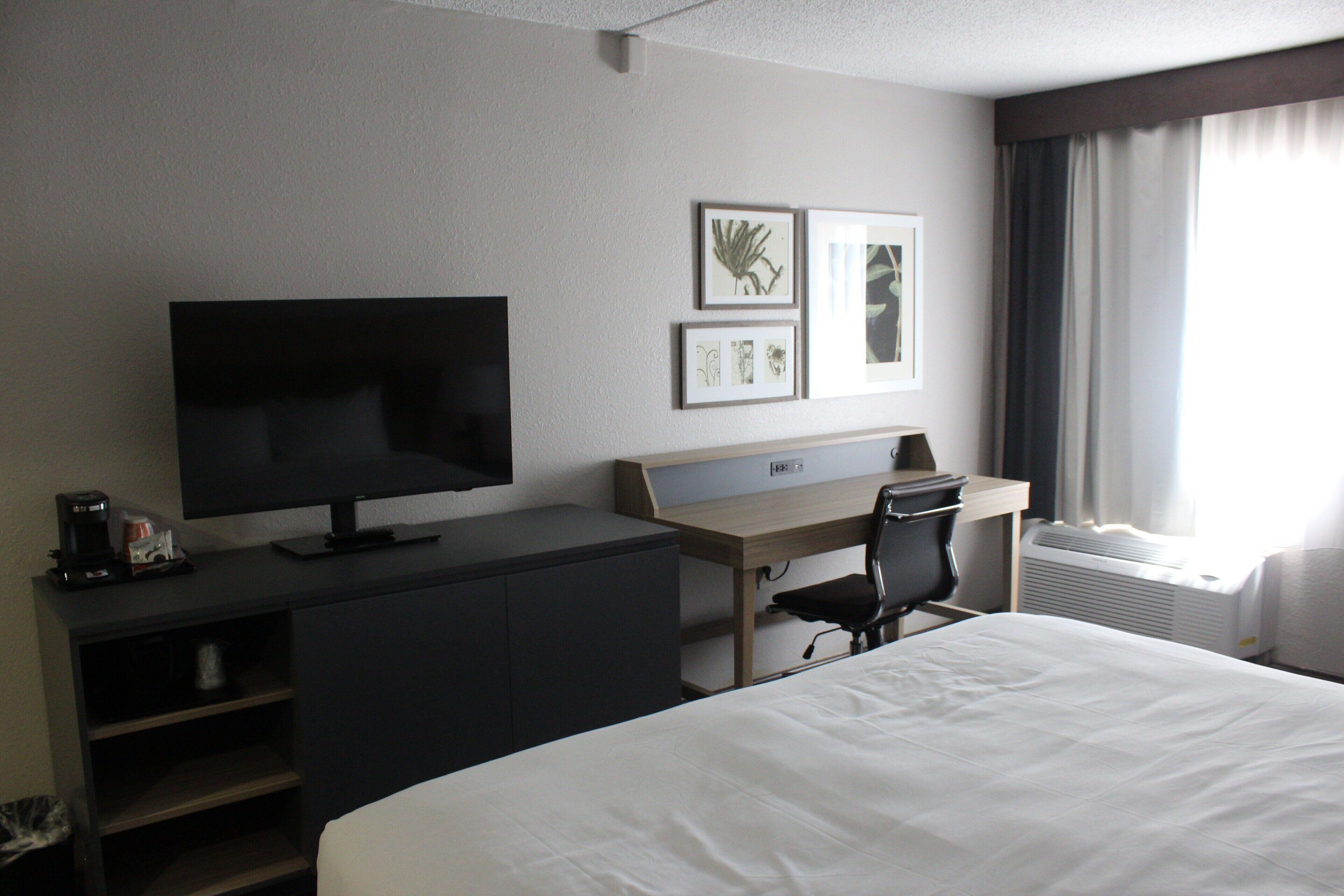 Habitación de hotel con cama, escritorio con silla, televisión y cuadros en la pared.