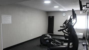 A fitness center with exercise equipment, a clock on the wall, and a sign with safety rules.