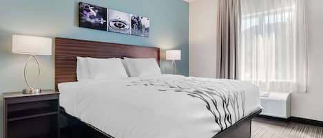 Quarto de hotel com uma cama grande, duas mesas de cabeceira com abajures, uma obra de arte na parede e uma janela com cortinas.