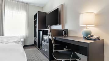 A hotel room with a bed, a desk with a chair, a television, a lamp, and a telephone.
