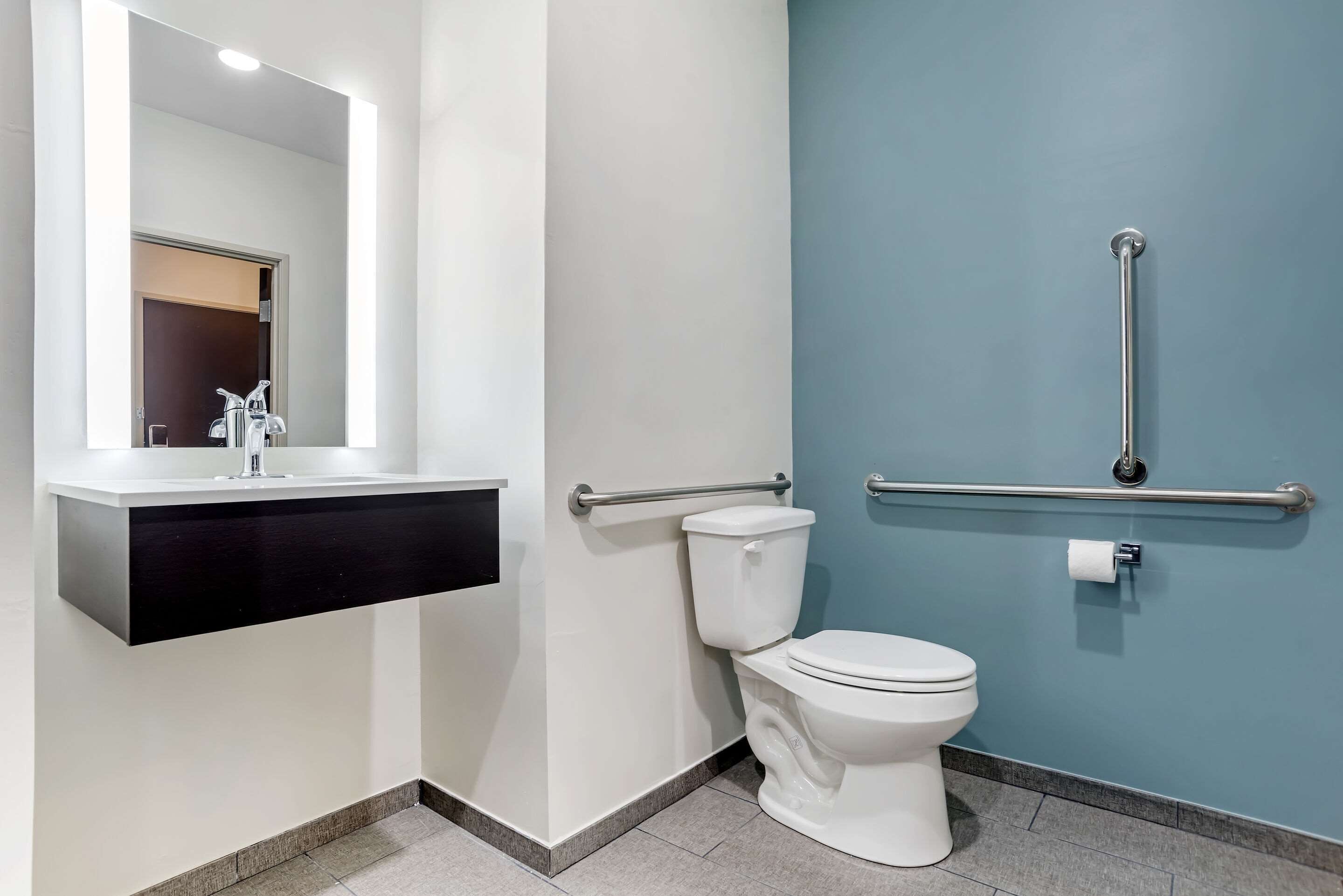 Une salle de bain moderne avec un lavabo blanc, des toilettes et une barre d’appui.