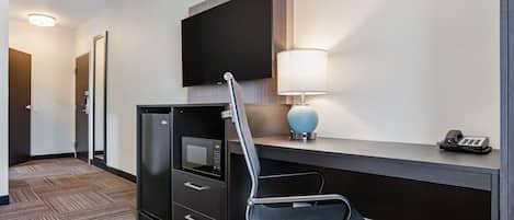 A hotel room with a desk, a chair, a microwave, a telephone, and a television mounted on the wall.