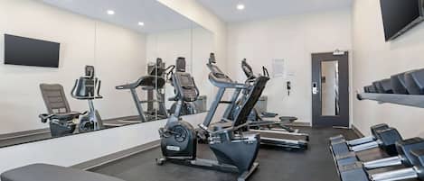 Een sportschool met cardioapparatuur, banken en gewichten.