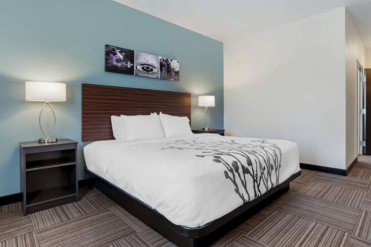 A hotel room with a large bed, two bedside tables with lamps, a headboard, and a wall with three framed pictures.