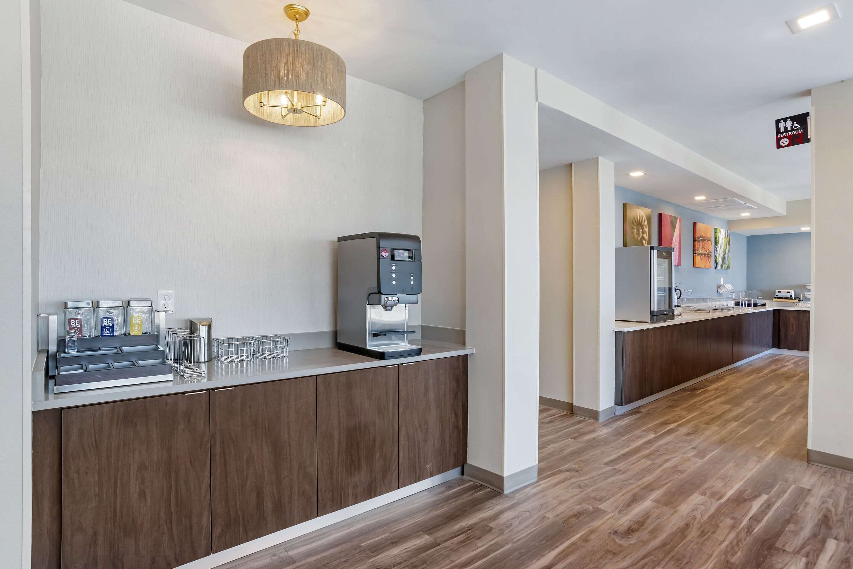 A modern hotel lobby with a coffee station, a water dispenser, and a sign indicating accessible facilities.