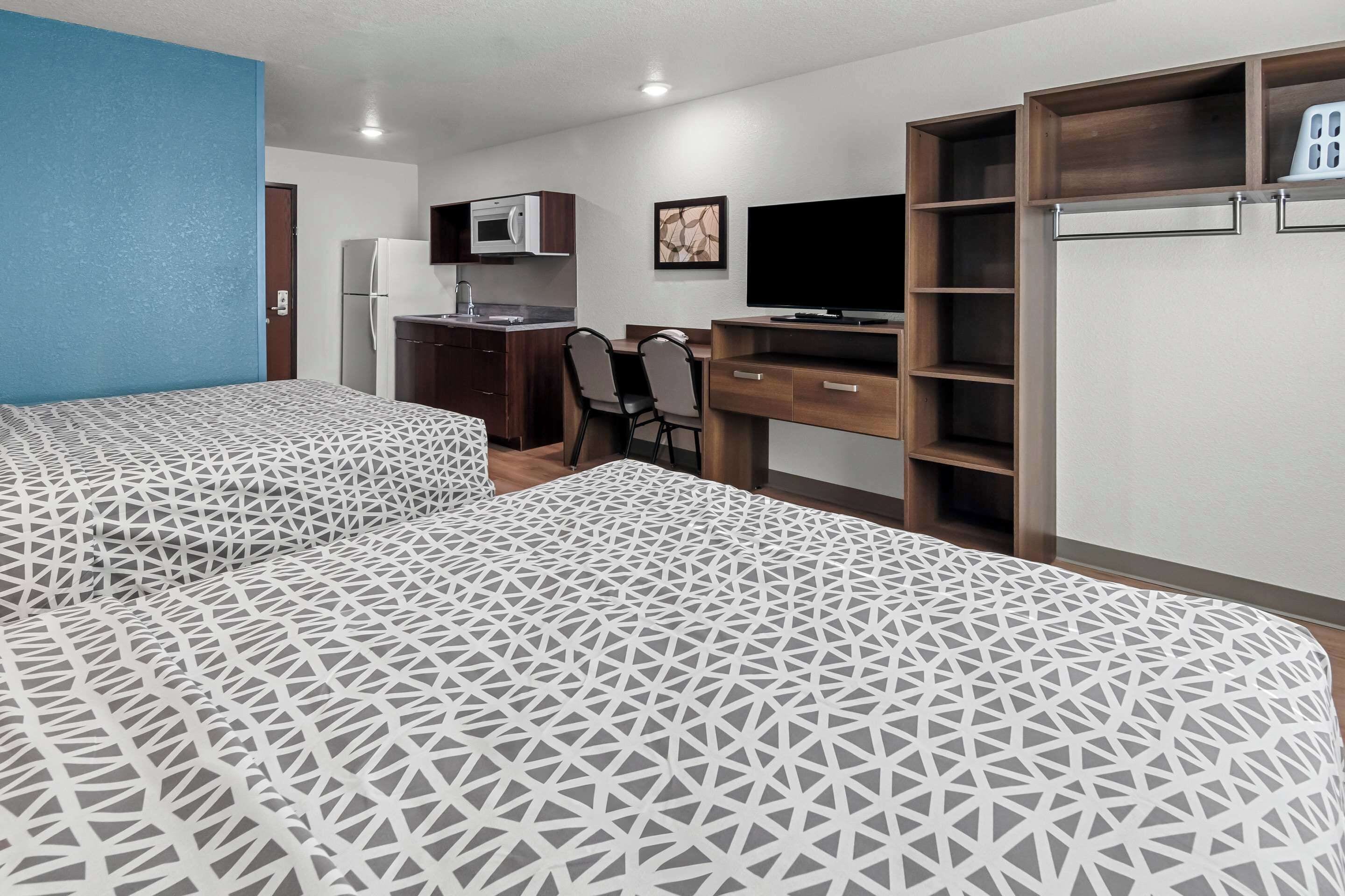 A hotel room with two beds, a kitchenette, a desk, a TV, and a wardrobe.