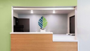 A reception area with a wooden counter, a white sink, and a green wall. - Woodspring Suites Waco South (Waco)