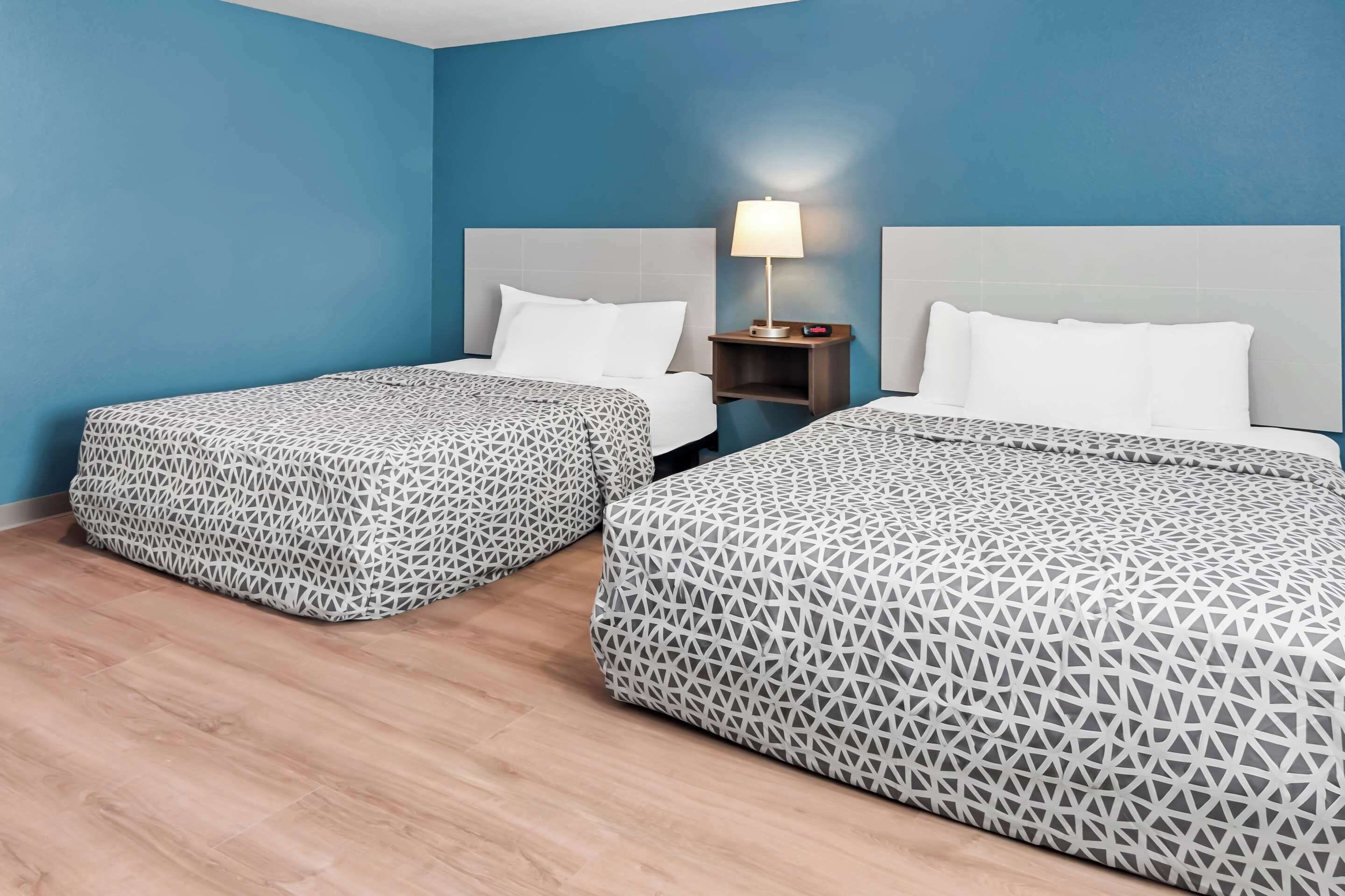 Une chambre d’hôtel avec deux lits, chacun recouvert d’une couvre-lit à motifs, une table de chevet avec une lampe et un mur bleu.