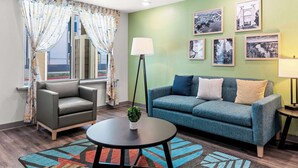 A modern living room with a grey leather sofa, a teal sofa with cushions, a round coffee table, and a colorful rug. - Woodspring Suites Waco South (Waco)