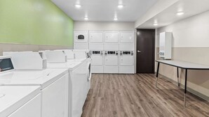 A laundry room with multiple washers and dryers, a table, and a door. - Woodspring Suites Waco South (Waco)