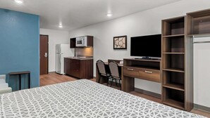 A compact hotel room with a bed, kitchenette, desk, and TV. - Woodspring Suites Waco South (Waco)