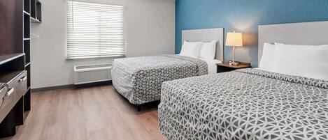 A hotel room with two beds, a desk, a chair, a wardrobe, and a window with blinds.