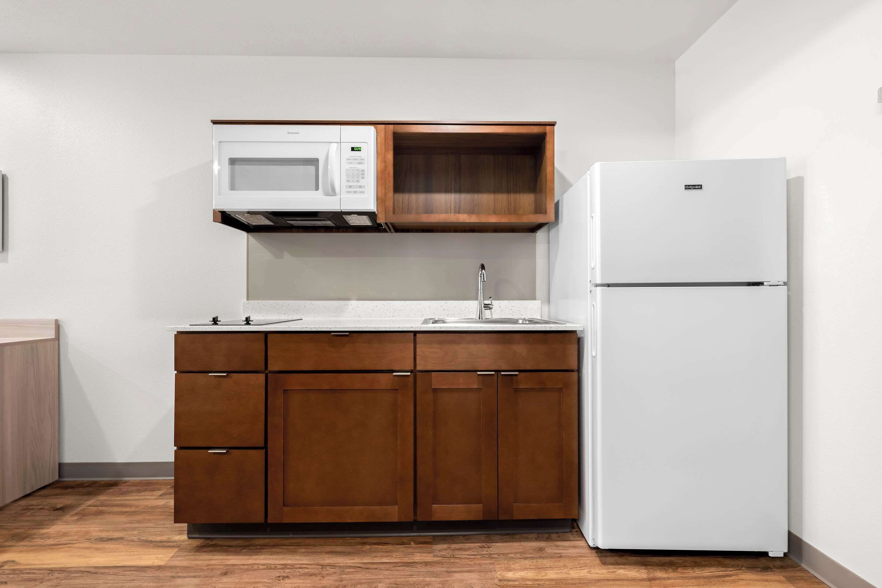 A compact kitchen with a microwave, wooden cabinets, and a white refrigerator.