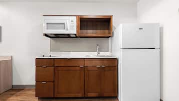 A compact kitchen with a microwave, wooden cabinets, and a white refrigerator.