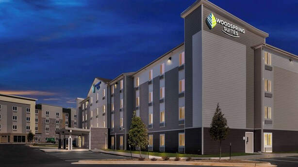 Un hôtel moderne doté d’un toit plat, de plusieurs étages et d’une enseigne bien visible indiquant « Woodspring Suites ».