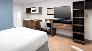 Une chambre d’hôtel comprenant un lit, un bureau avec une chaise, une télévision, un four à micro-ondes et une armoire.