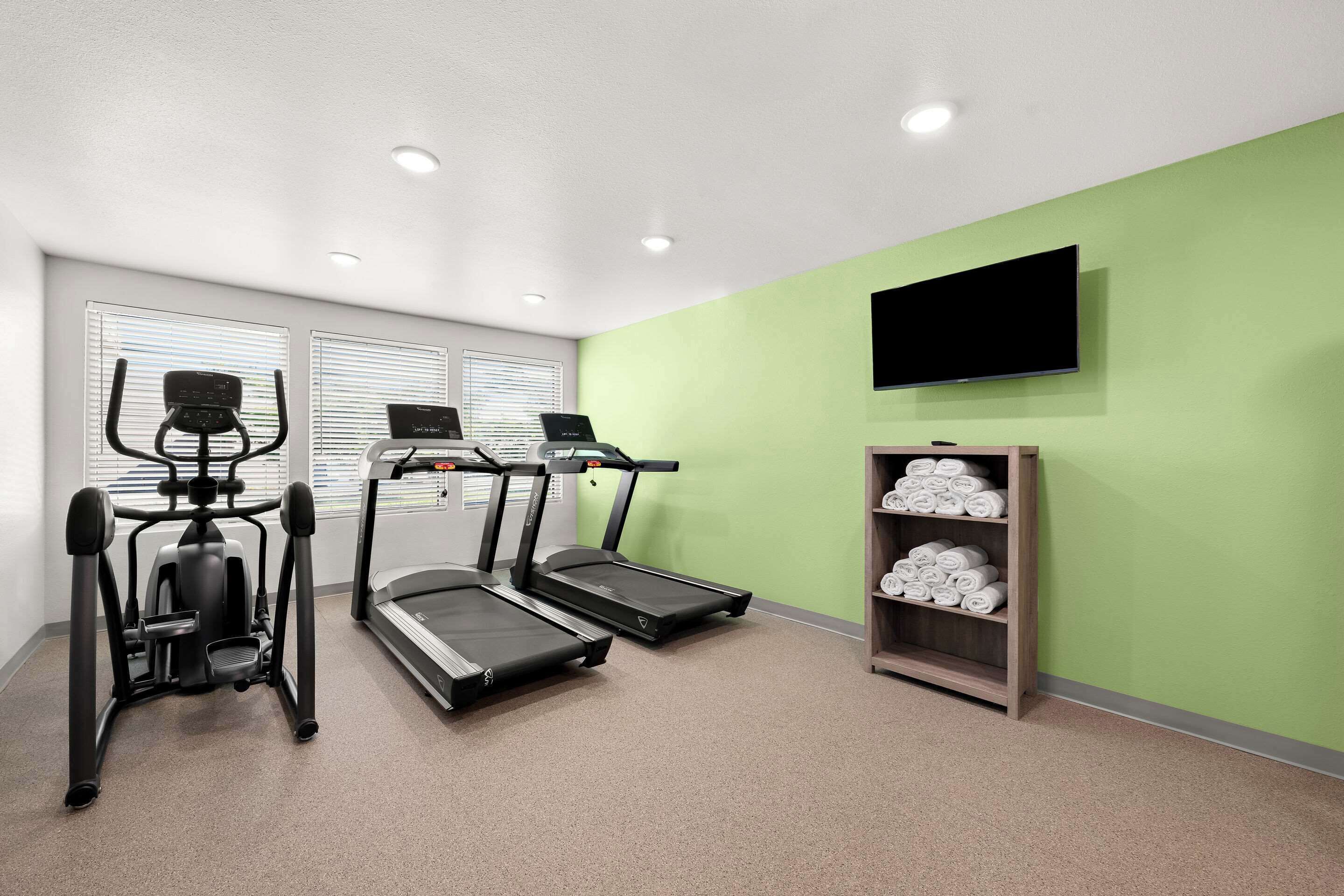 Un gimnasio equipado con cintas de correr, una bicicleta estática y un televisor en la pared.