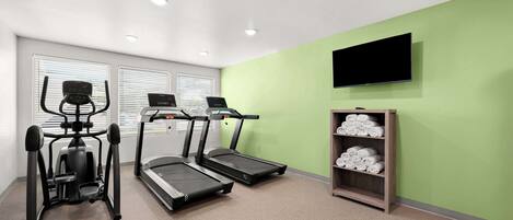 Ein Fitnessraum mit Laufbändern, einem Ergometer und einem Fernseher an der Wand.