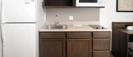 A compact kitchen with a white refrigerator, a microwave, a sink, and wooden cabinets.
