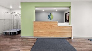 Un comptoir d’accueil avec un mur d’accent vert, un logo et un chariot à roulettes.