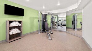Une salle de sport équipée de matériel d’exercice, d’un téléviseur et d’une étagère où sont rangées des serviettes.