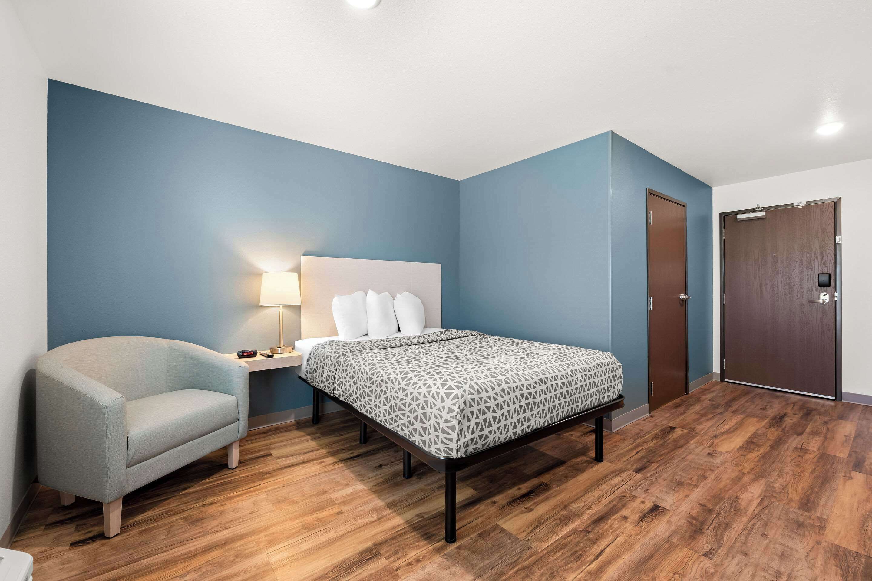 A bedroom with a bed, a chair, a nightstand, a lamp, and a wardrobe.
