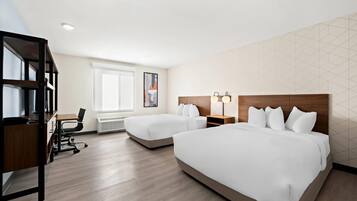 A hotel room with two beds, a desk, a chair, and a bookshelf.