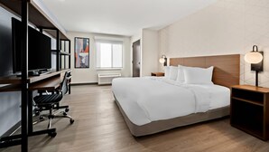 A modern hotel room with a large bed, a desk with a chair, a TV, and a bedside table with lamps.