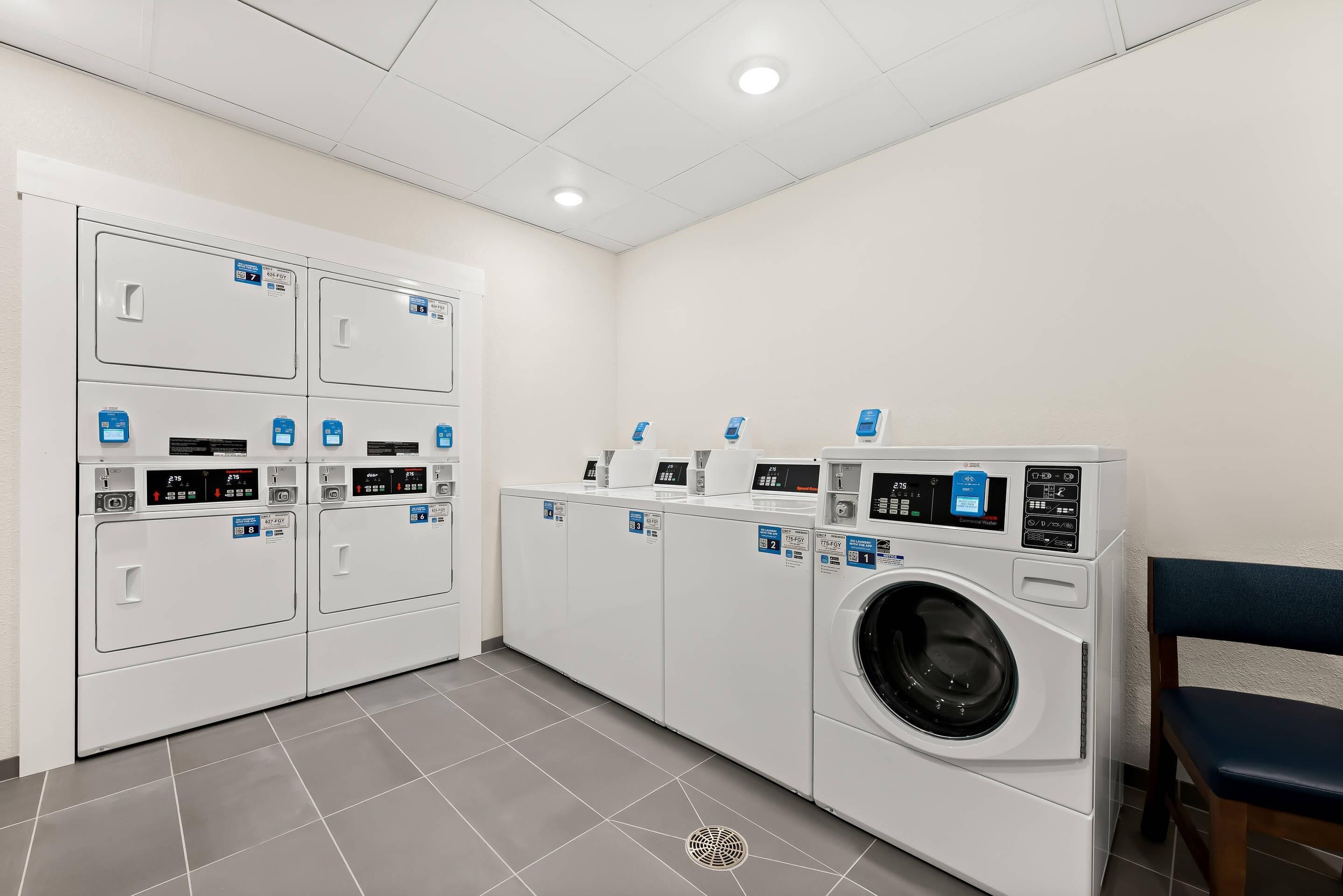 A laundry facility with multiple washing machines and dryers, a tiled floor, and a ceiling with recessed lighting.