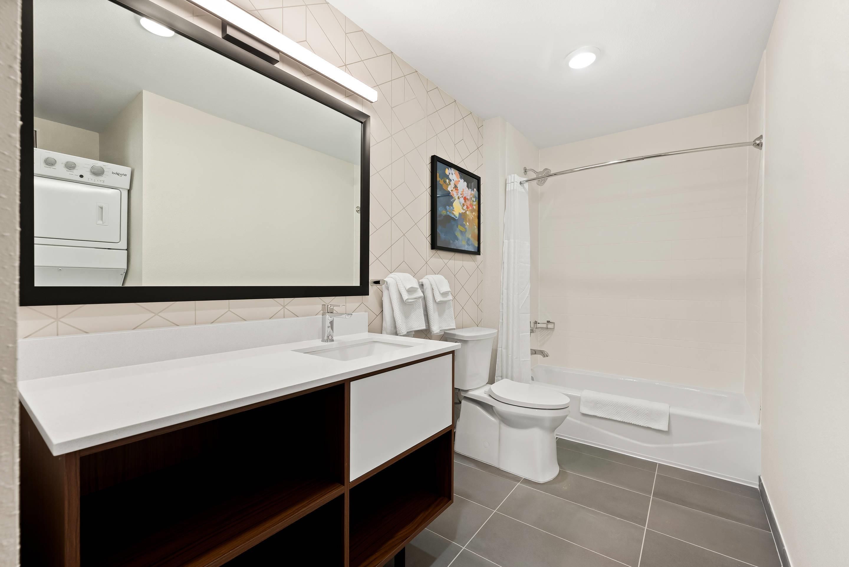 Un baño moderno con un espejo grande, un lavamanos blanco, un inodoro y una bañera.