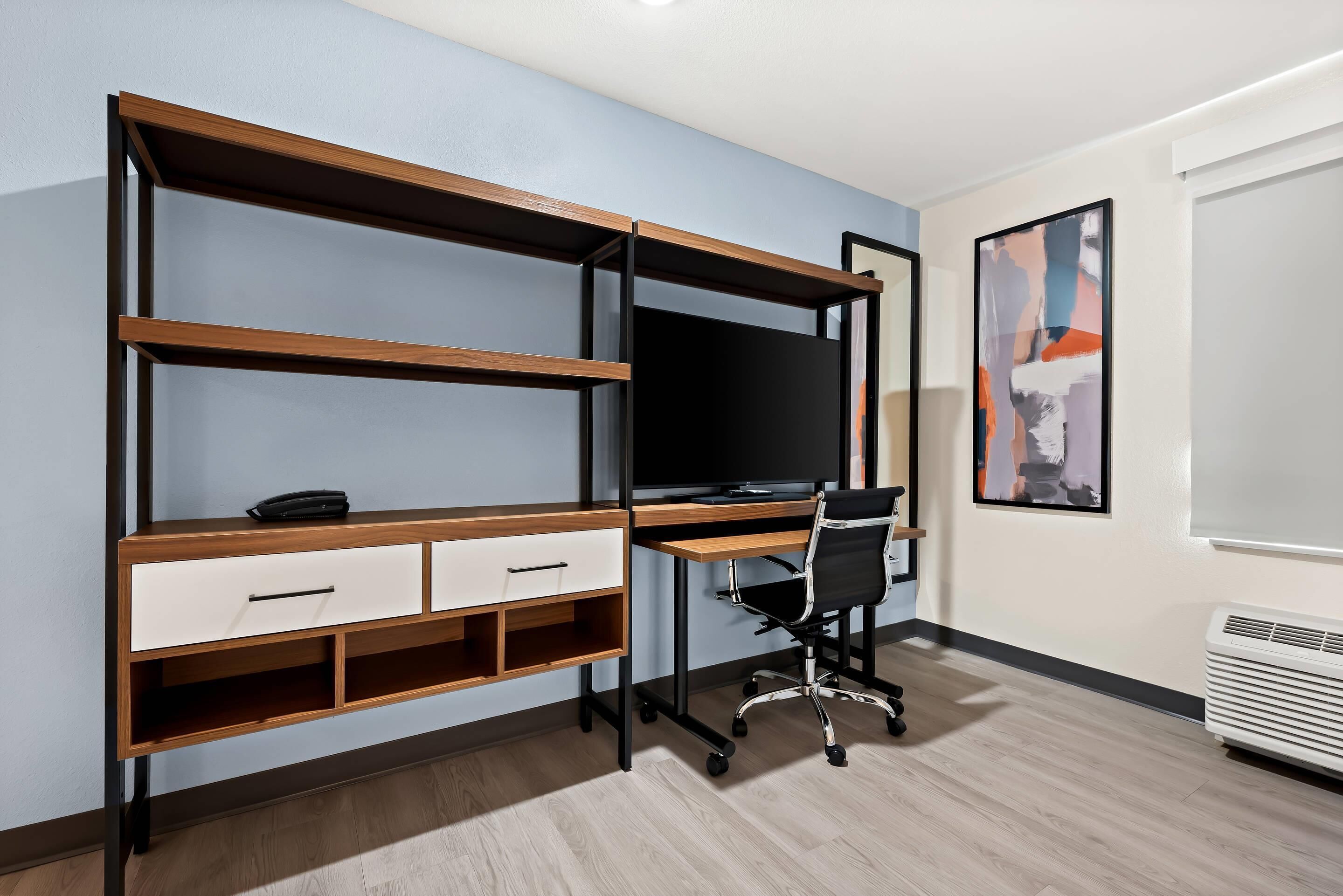 Un espacio de oficina moderno con un escritorio de madera, dos cajones, una silla de oficina negra y un monitor de pantalla plana grande.
