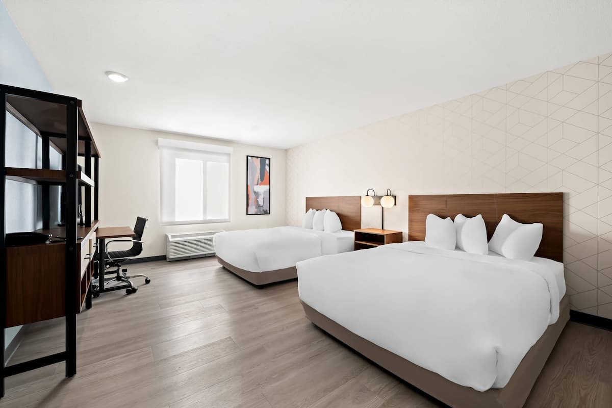 A hotel room with two beds, a desk, and a bookshelf.